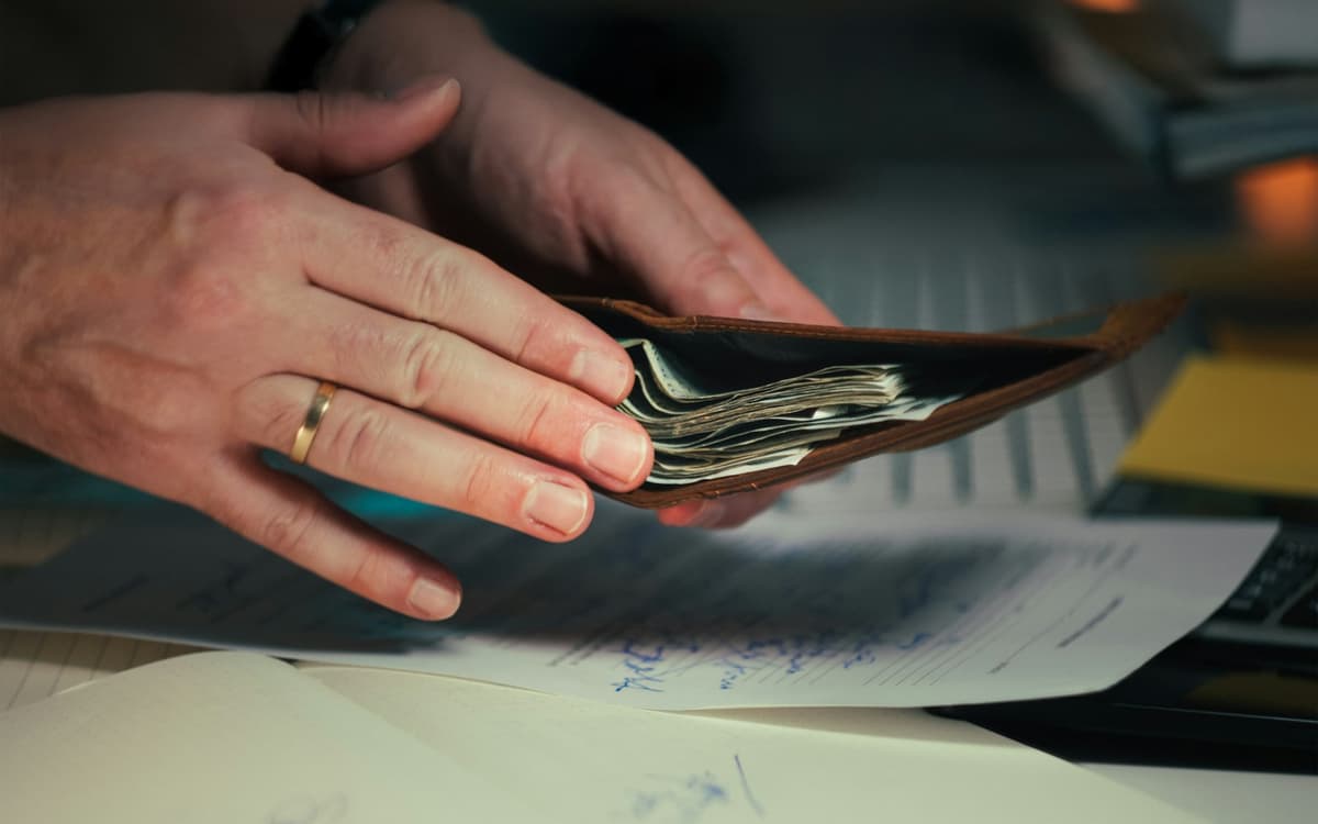 Hands counting cash over a wallet and papers