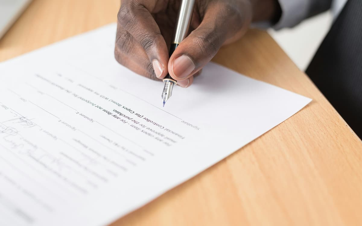A hand signing a document with a pen