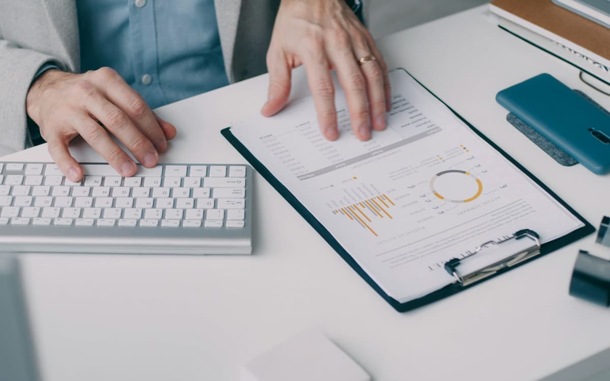 Hands on a keyboard beside a clipboard of financial charts