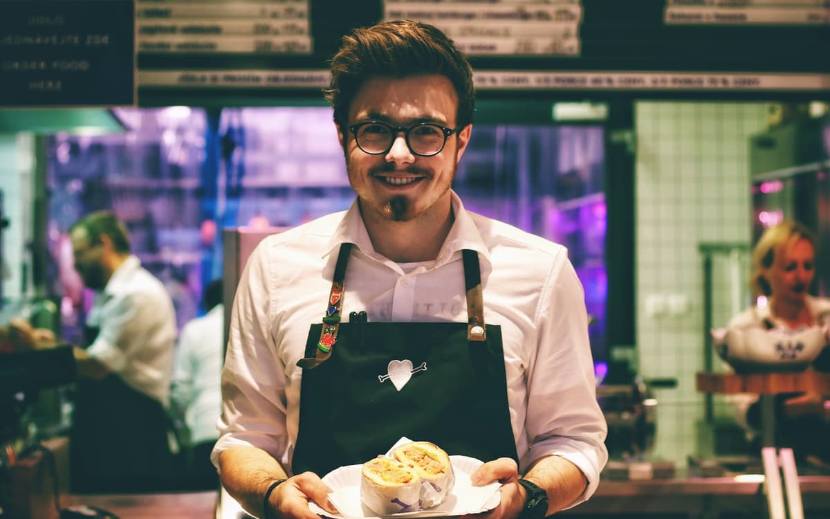 A smiling waiter in an apron holding a plate