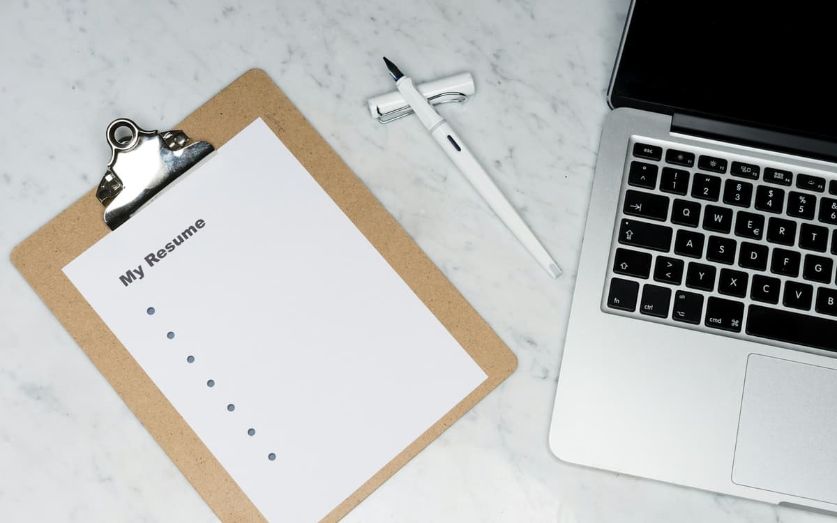 A blank CV on a clipboard beside a laptop