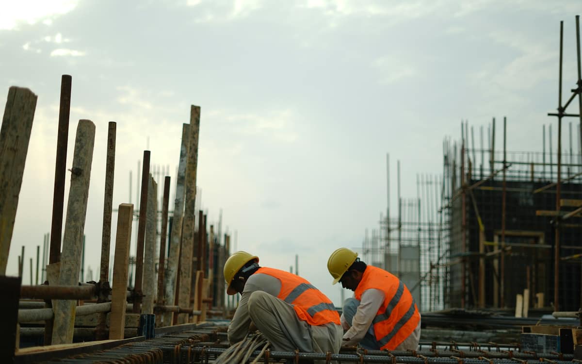 Two workers in hard hats and orange vests tying steel on a construction site