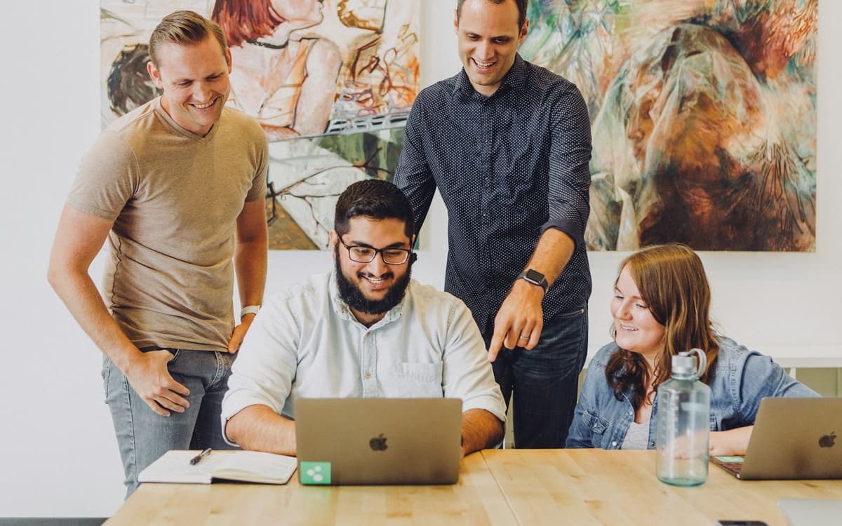 Four young colleagues smiling around a laptop