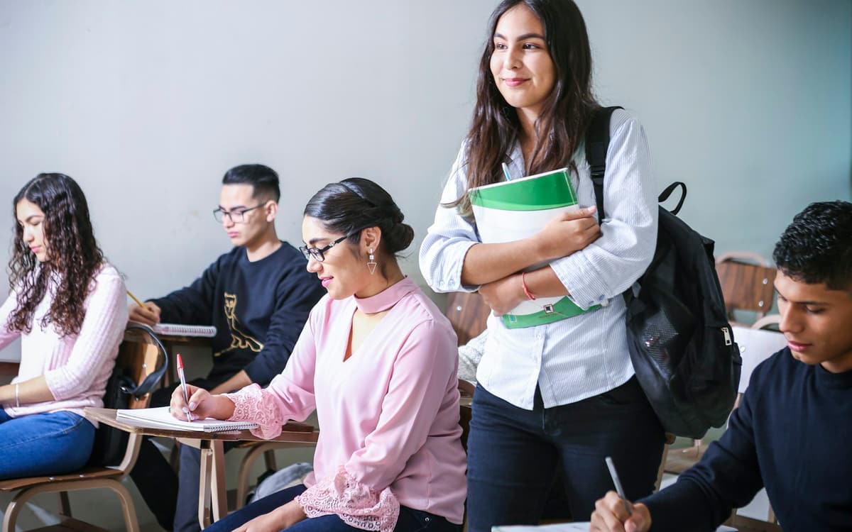 Students studying together in a classroom, one carrying textbooks