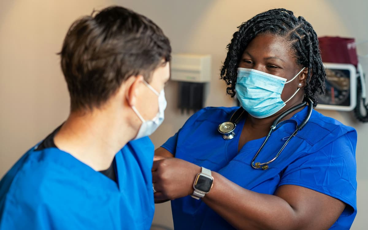 A nurse in blue scrubs and a mask attending to a patient